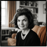 Black-and-white portrait of Jacqueline Kennedy Onassis wearing a three-strand pearl necklace and sunglasses on her head